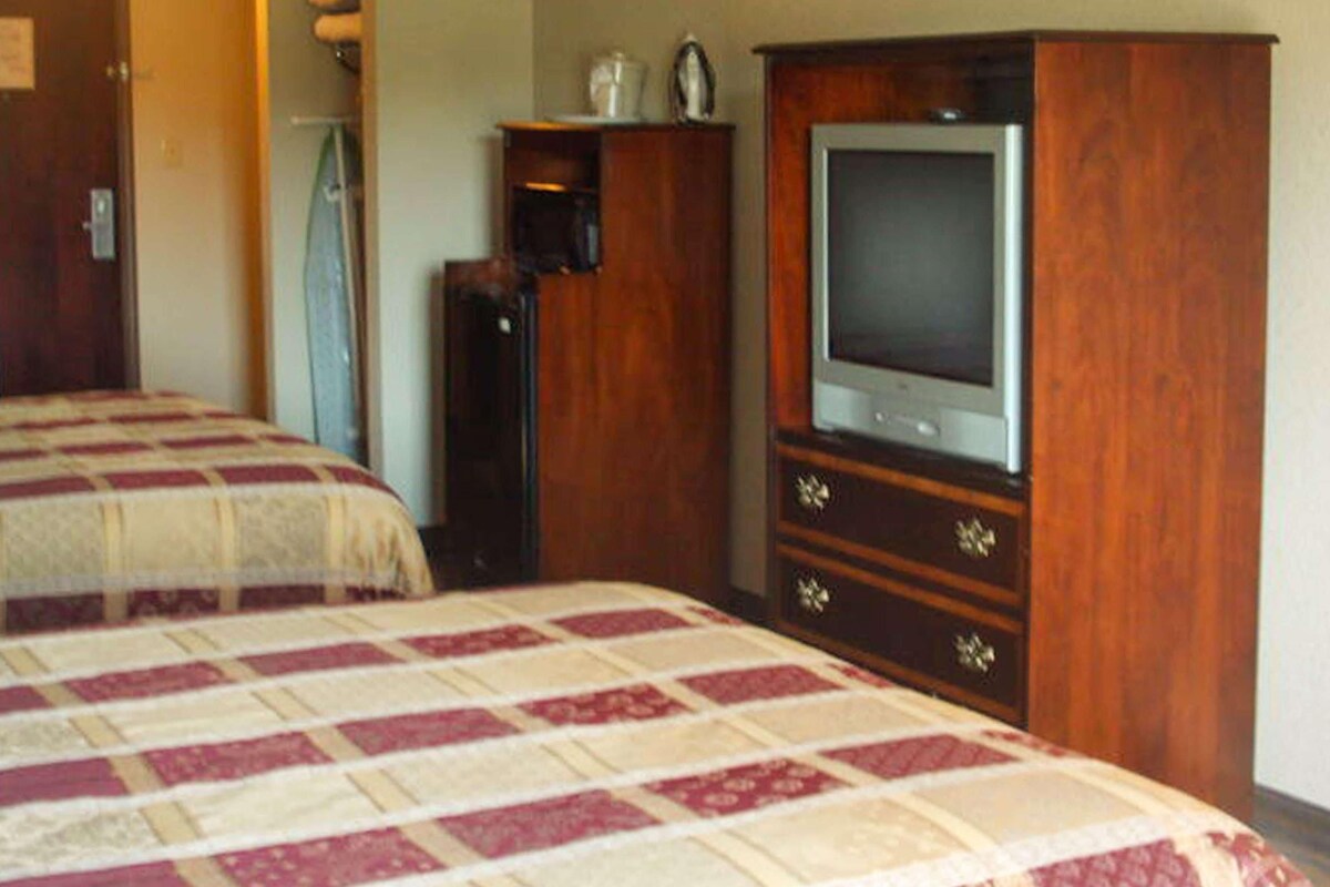 A hotel room with two beds, a wooden wardrobe, and a television.