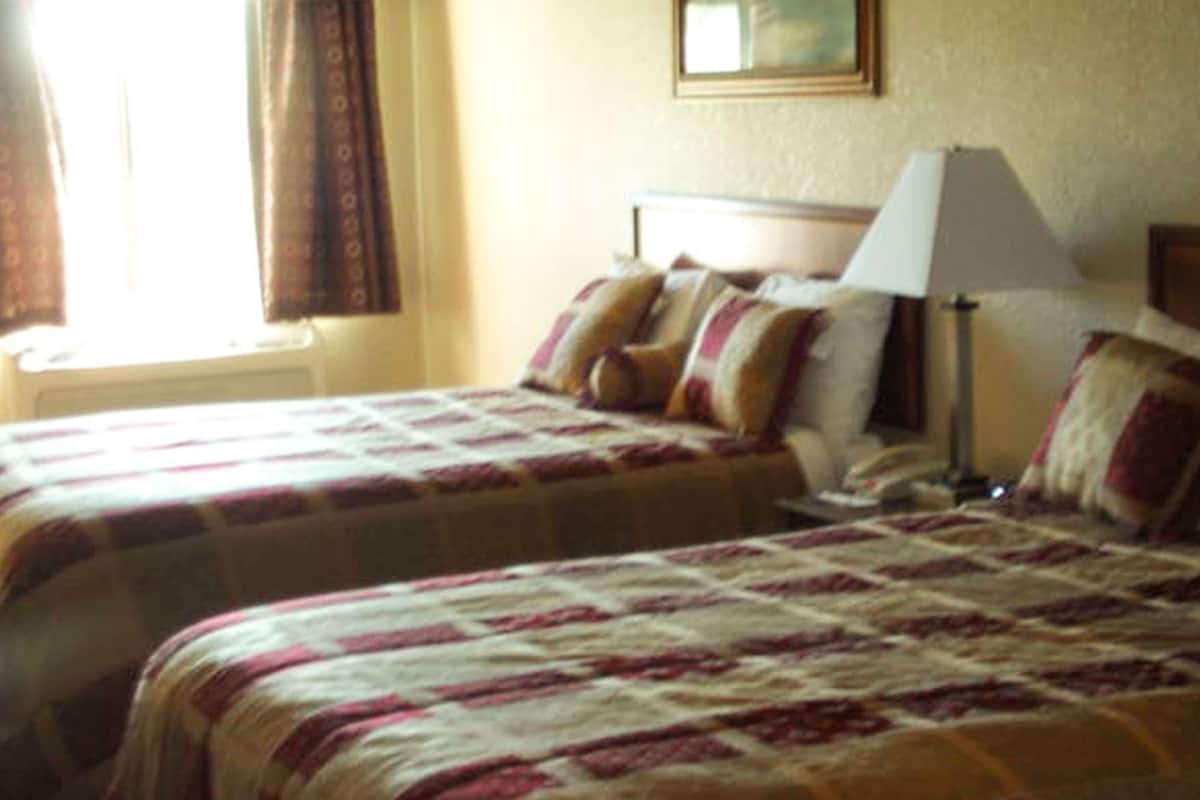 A hotel room with two beds, a bedside lamp, and a window with curtains.