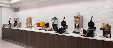 A modern hotel reception area with a long counter, various coffee machines, and a selection of beverages.