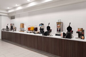 A modern hotel reception area with a long counter, various coffee machines, and a selection of beverages.