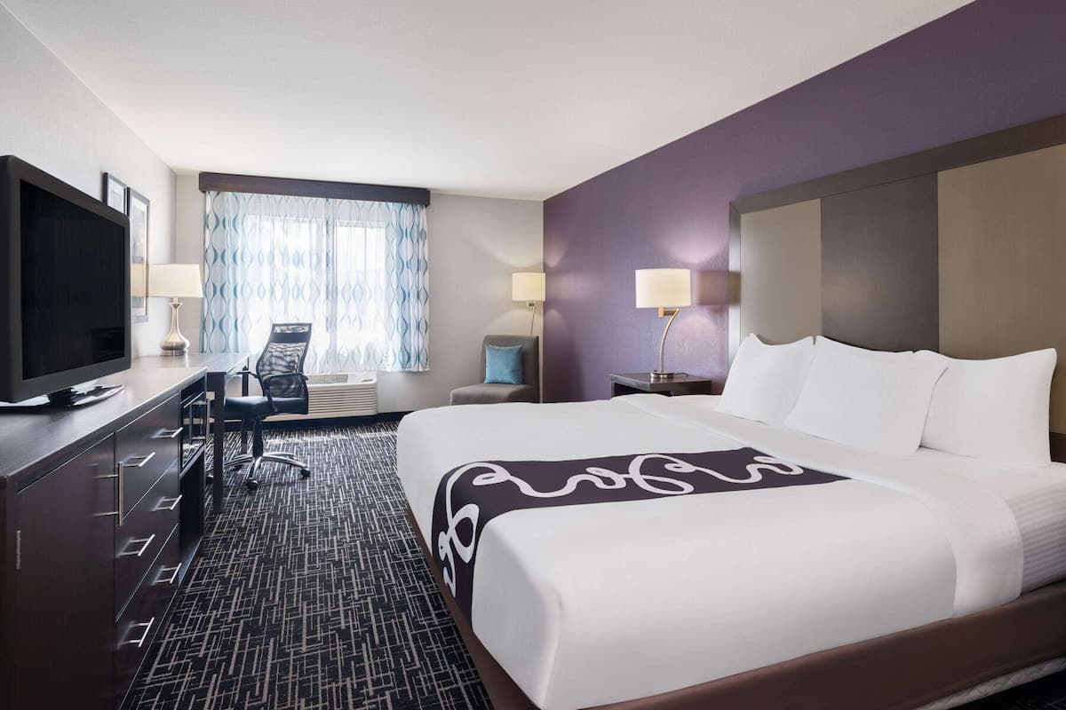 A hotel room with a large bed, a desk with a television, two lamps, and a chair.