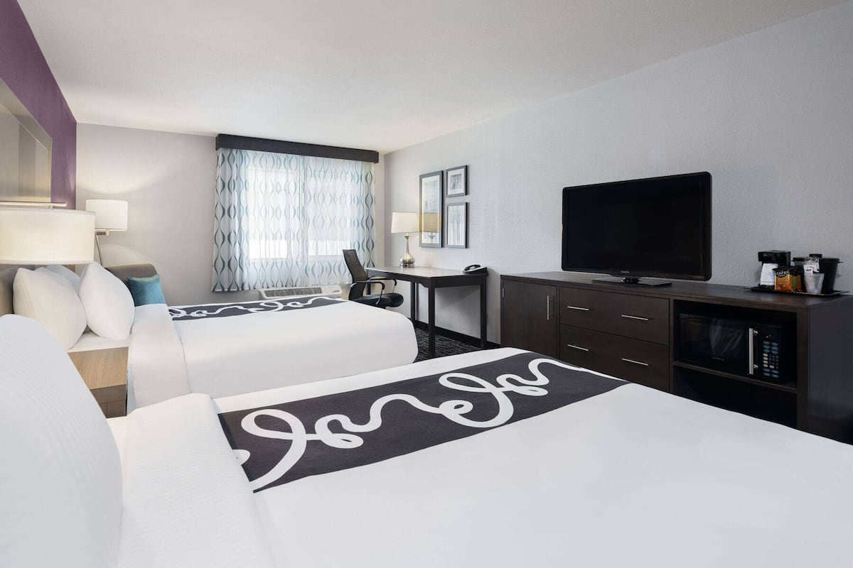 A hotel room with two beds, a desk, a television, and a minibar.