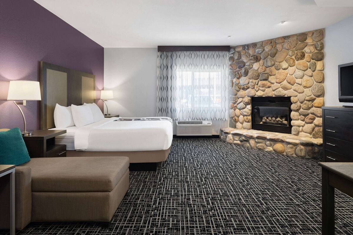 A hotel room with a bed, a seating area, a stone fireplace, and a television.