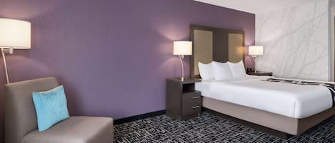Una habitación de hotel con una cama, una silla, una mesita de noche y dos lámparas.