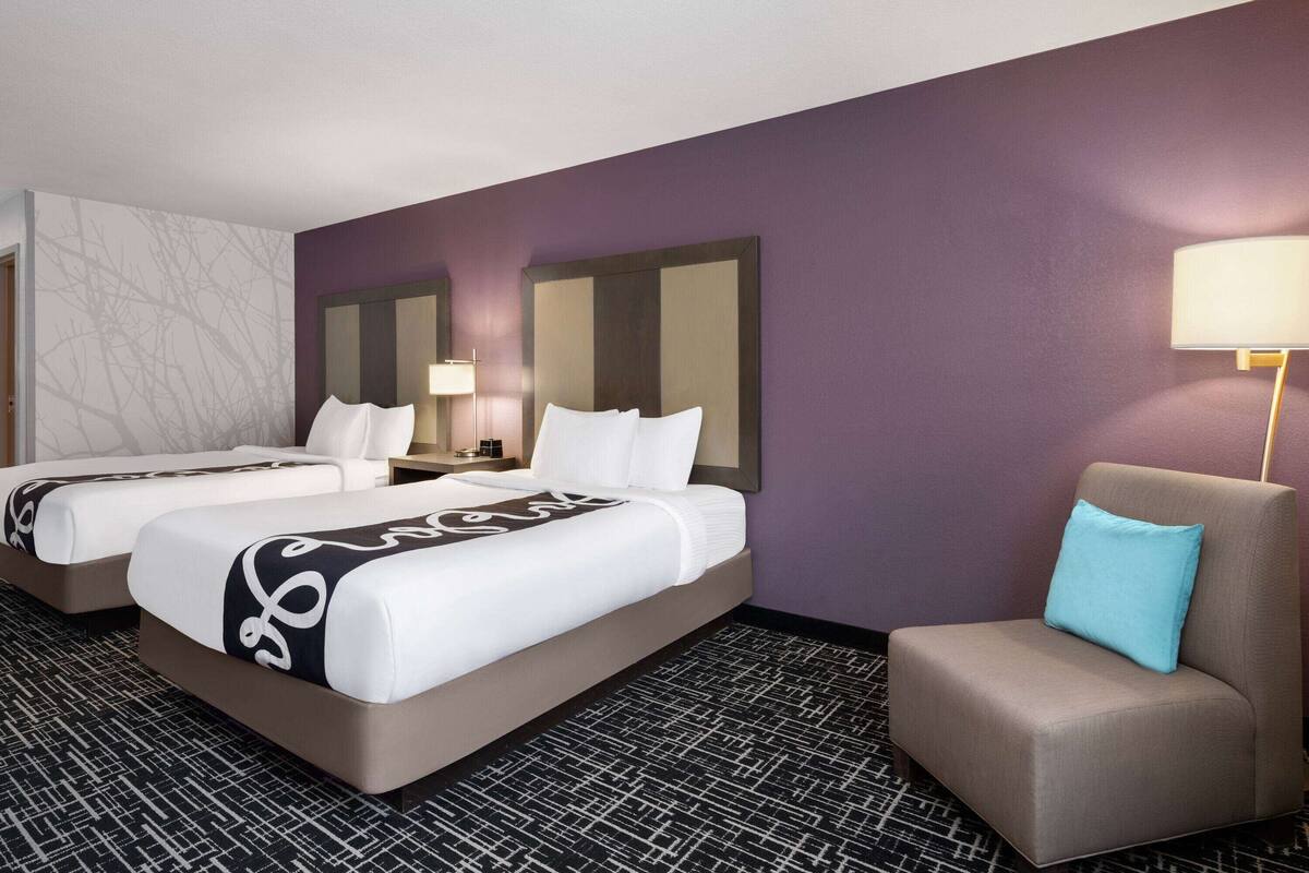 A hotel room with two beds, a seating area, and a nightstand with lamps.