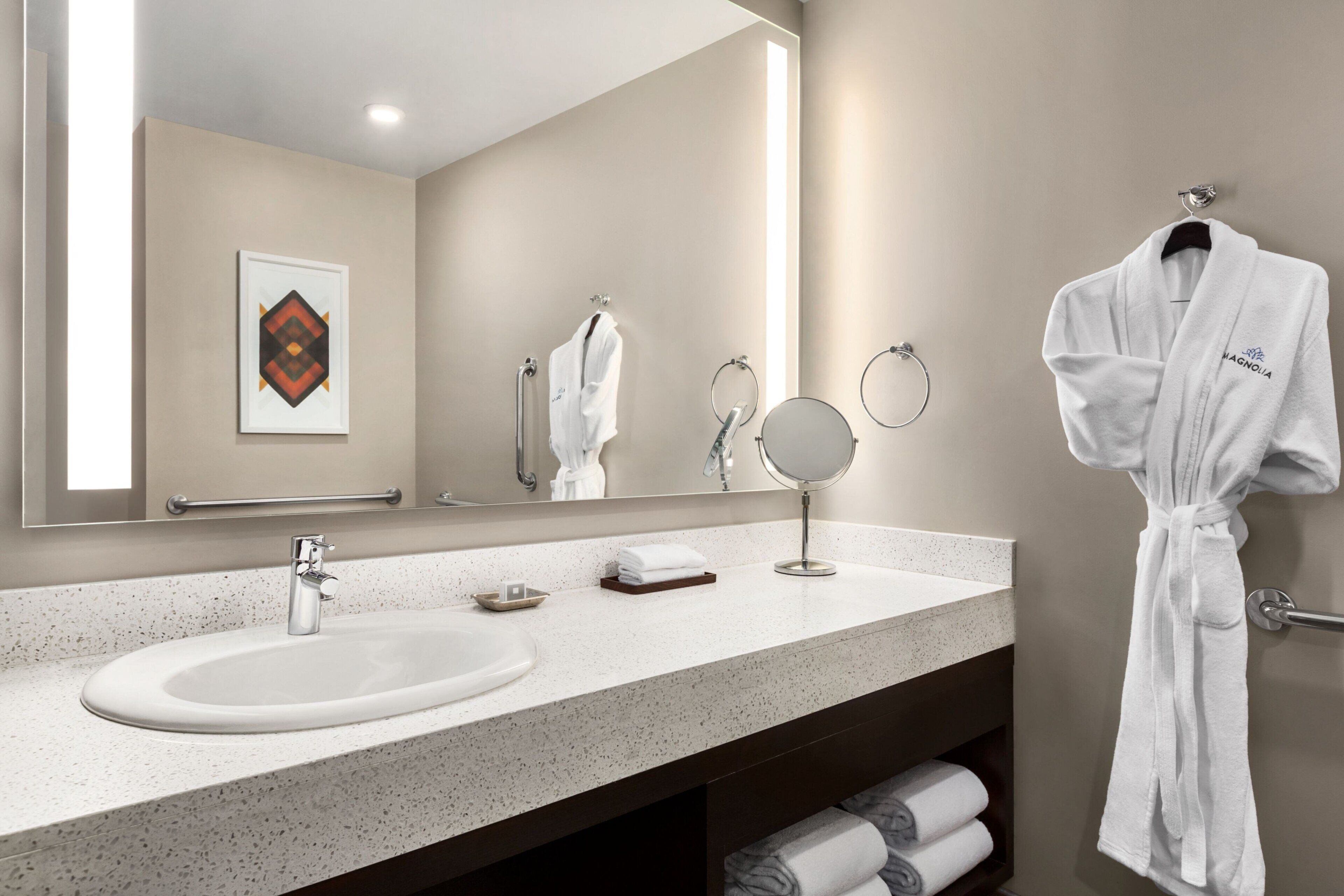 A modern bathroom with a large mirror, a sink, and a robe hanging on a rack.