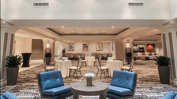 A spacious lobby with a high ceiling, large windows, and a central seating area with blue chairs and a round table. - Magnolia Hotel Denver, A Tribute Portfolio Hotel (Denver)