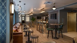 A modern bar area with high stools, a bar counter, and a seating area with a sofa and round tables. - Magnolia Hotel Denver, A Tribute Portfolio Hotel (Denver)