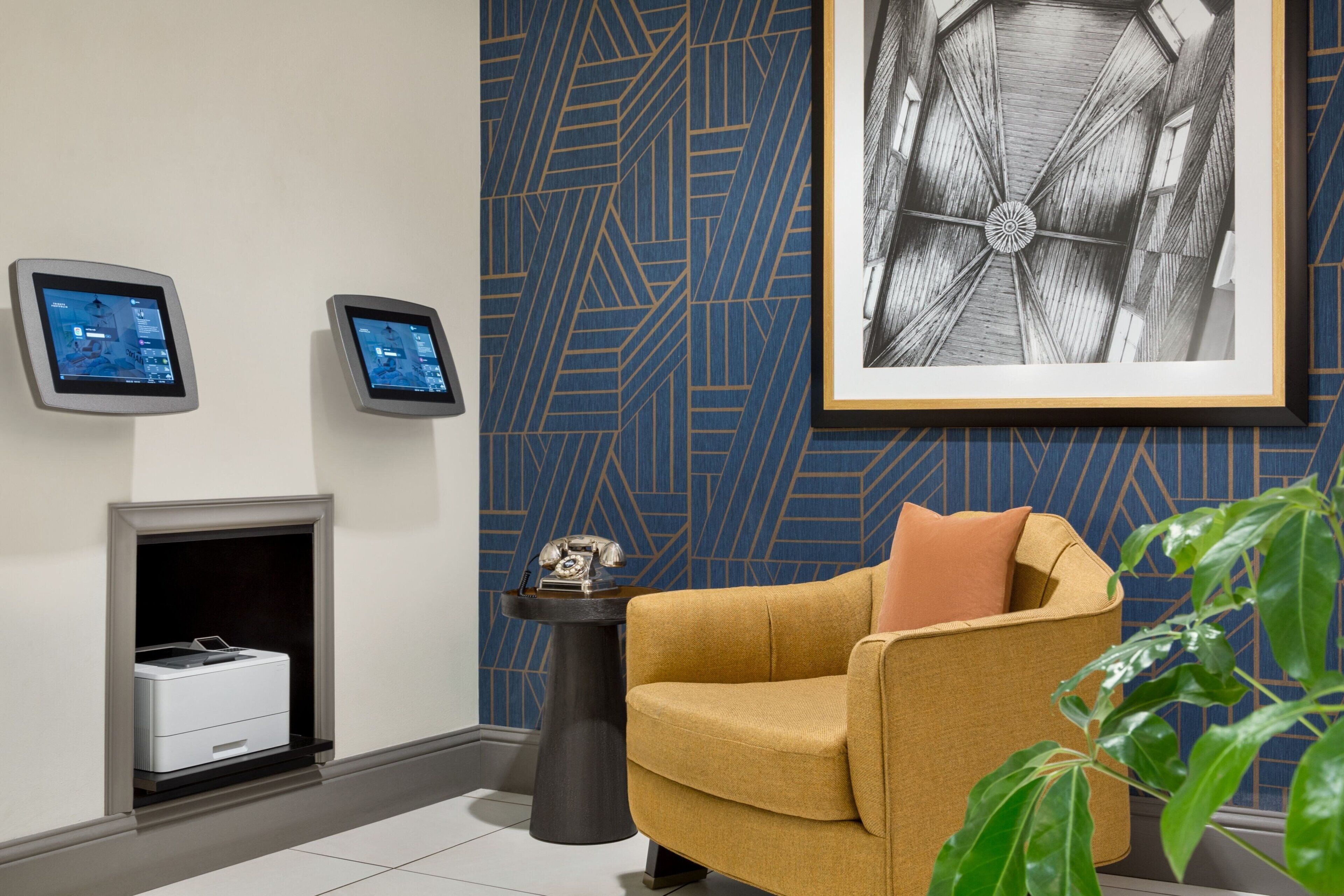 A modern lobby with a fireplace, two digital information kiosks, a framed artwork, and a comfortable seating area.