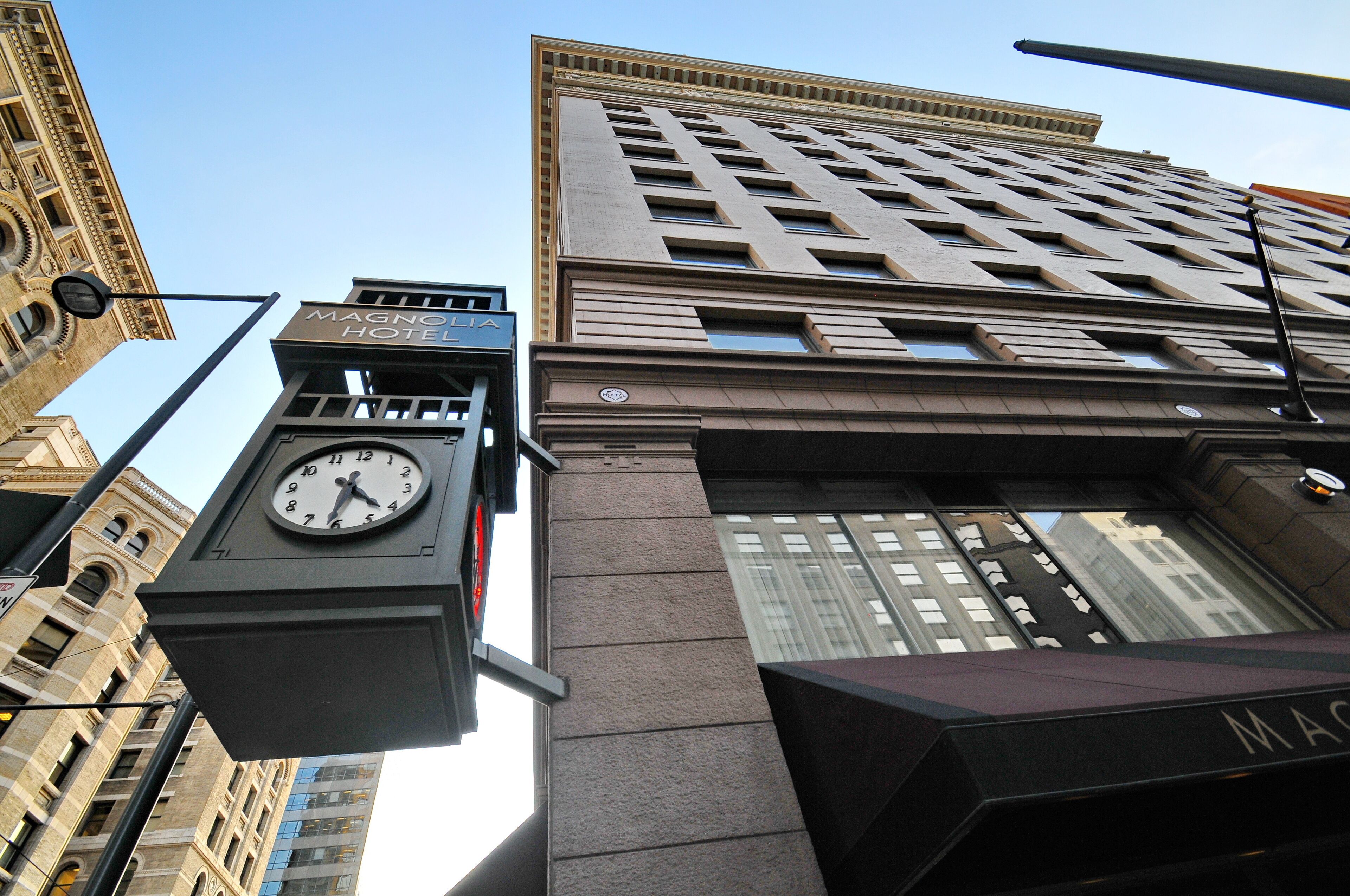 A clock tower with a sign for the Magnolia Hotel, part of a tall building with a modern design.