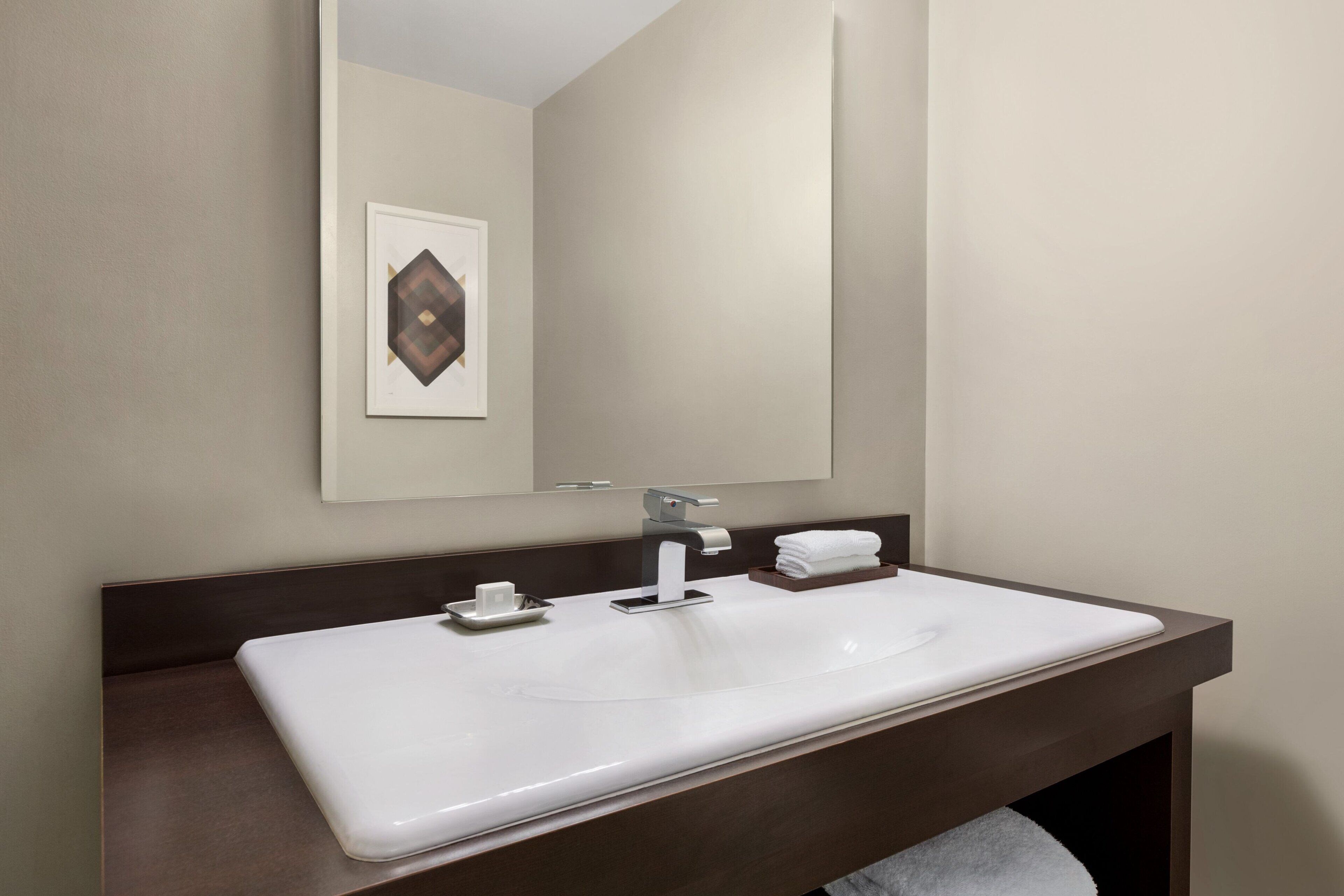 A modern bathroom with a white sink, dark brown vanity, and a large mirror.