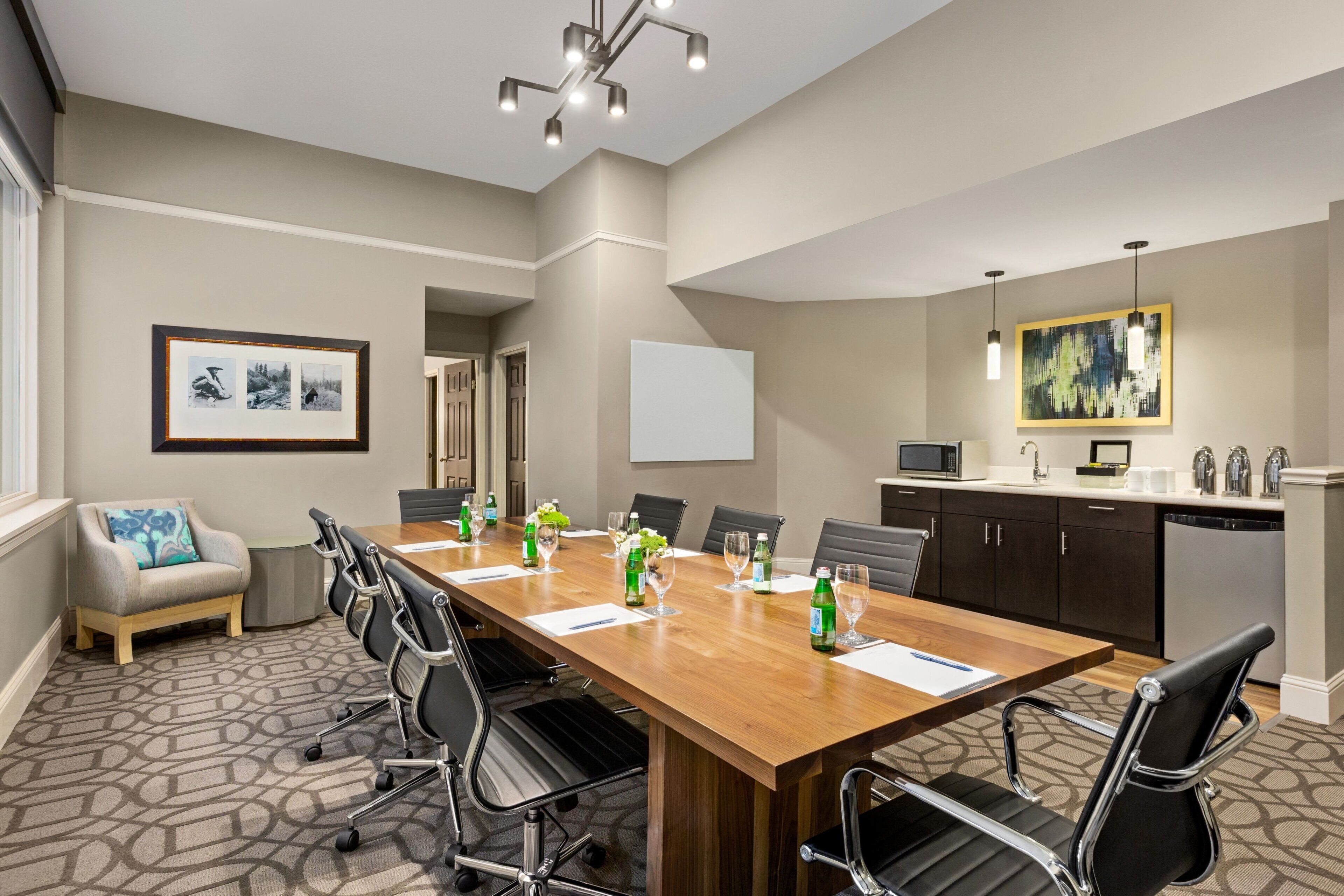 A conference room with a long table, chairs, a sofa, and a kitchen area with a microwave and sink.