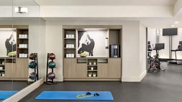 Un gimnasio moderno con equipo de ejercicio, colchonetas azules y un espejo grande.