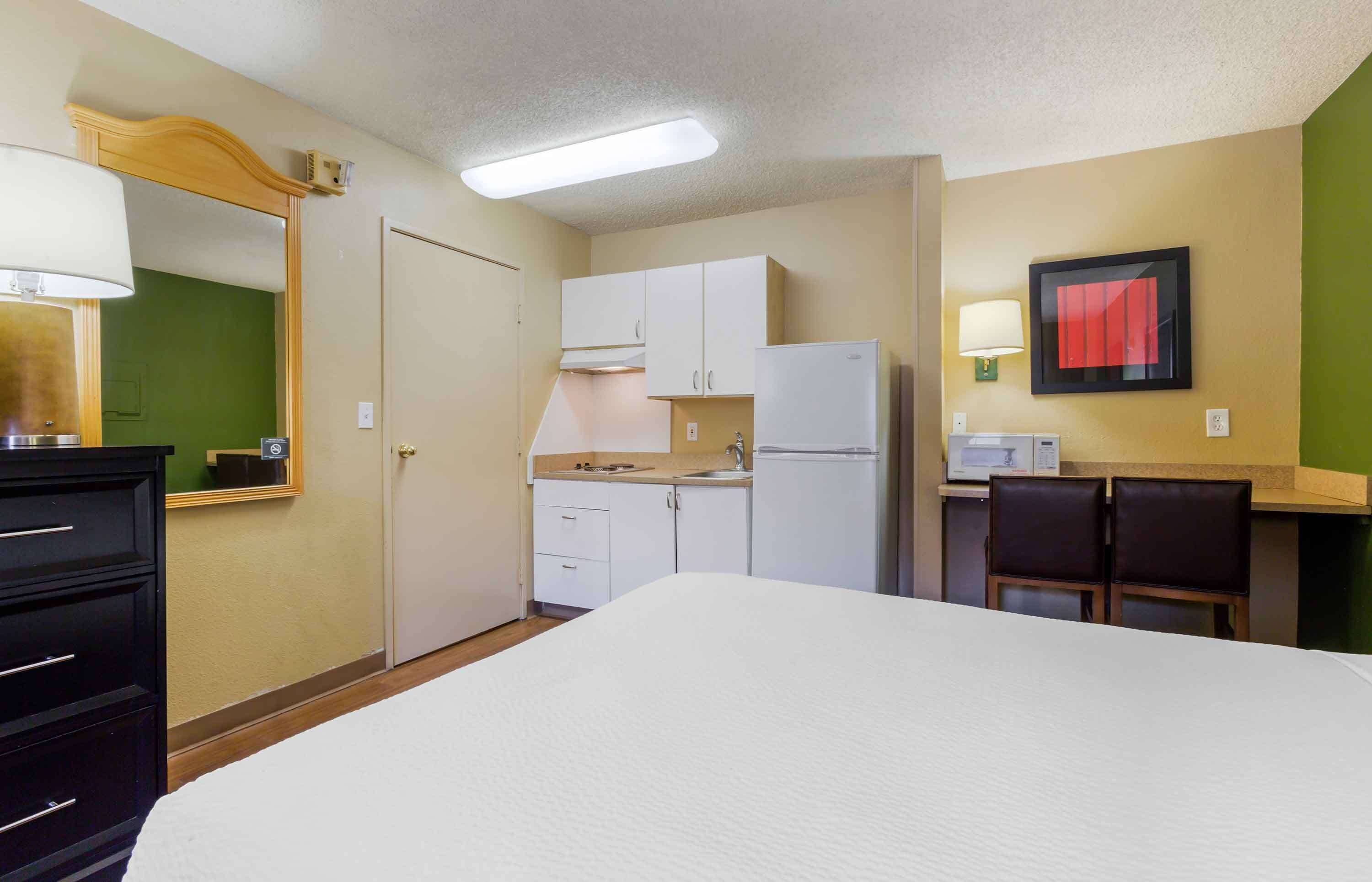 A hotel room with a bed, a dresser, a kitchenette, and a dining area.