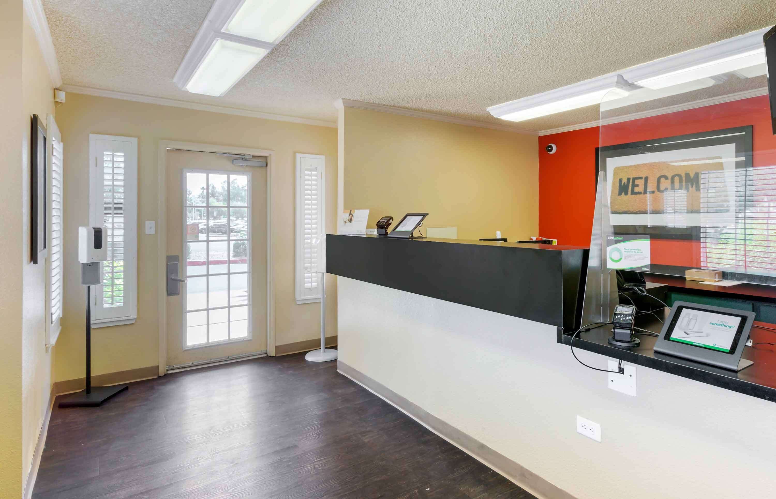 A reception area with a black reception desk, a 'WELCOME' sign, a digital display, and a door leading outside.