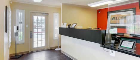 A reception area with a black reception desk, a 'WELCOME' sign, a digital display, and a door leading outside.