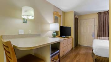Una habitación de hotel con kitchenette, televisión, cama y una puerta con cortinas.