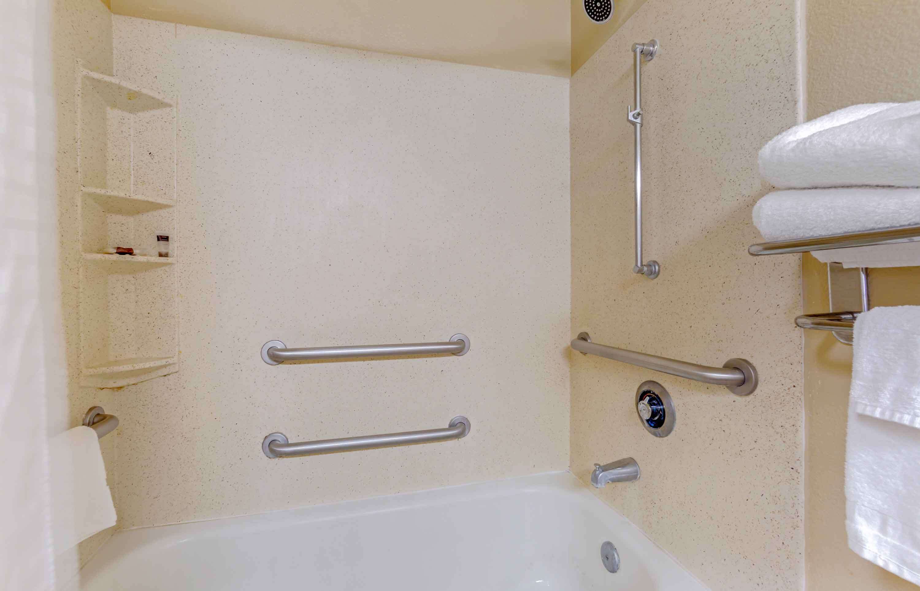 A bathroom with a bathtub, grab bars, shelves, and a towel rack.