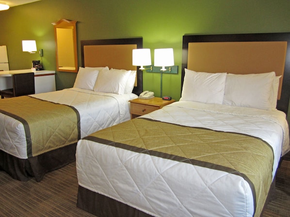 Habitación de hotel con dos camas, un escritorio, una silla, un espejo y dos lámparas de noche.