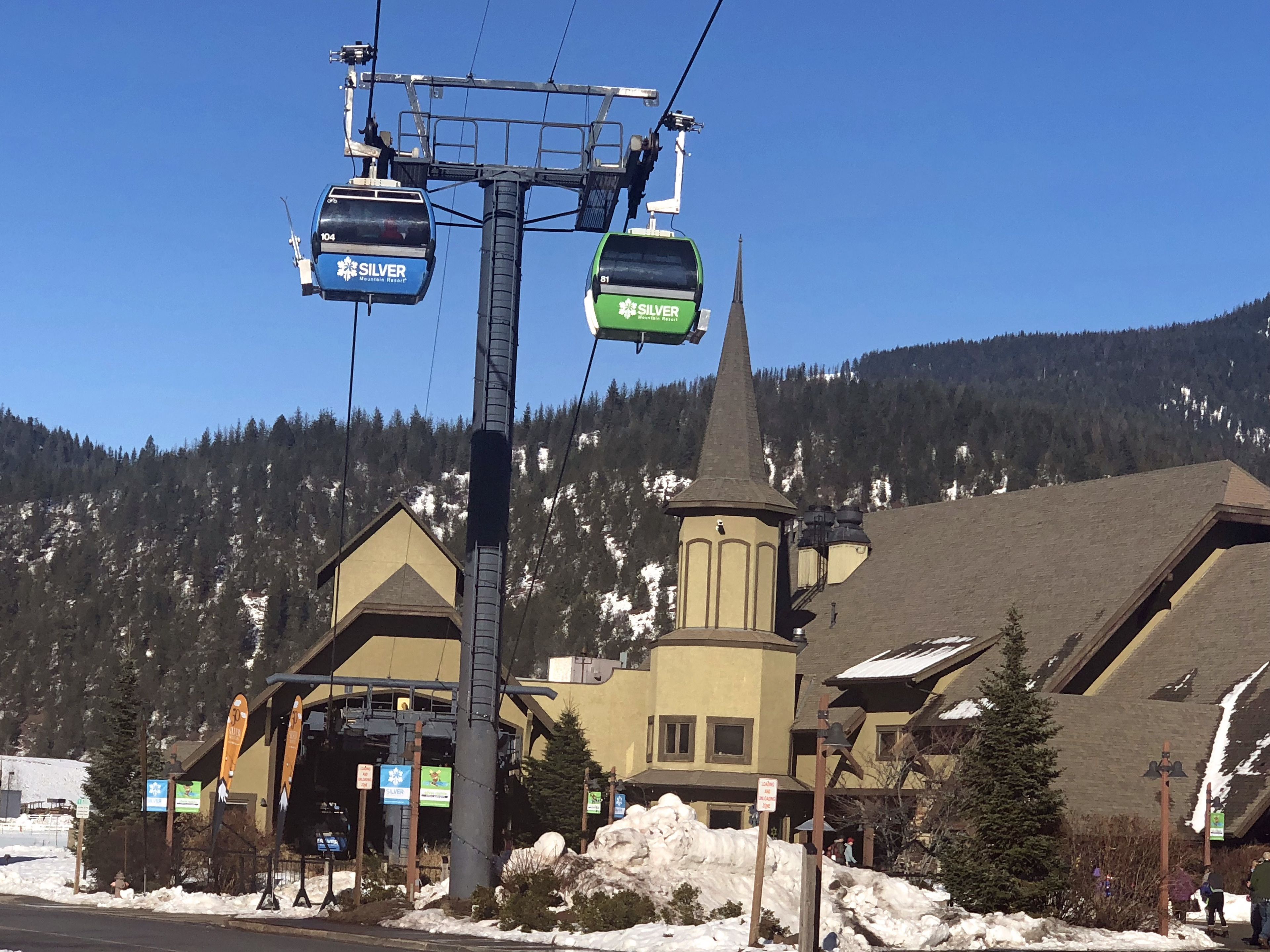 Un télésiège avec des cabines portant les inscriptions « SILVER » et « SILVER 81 », avec en arrière-plan une montagne et un bâtiment ressemblant à une église.