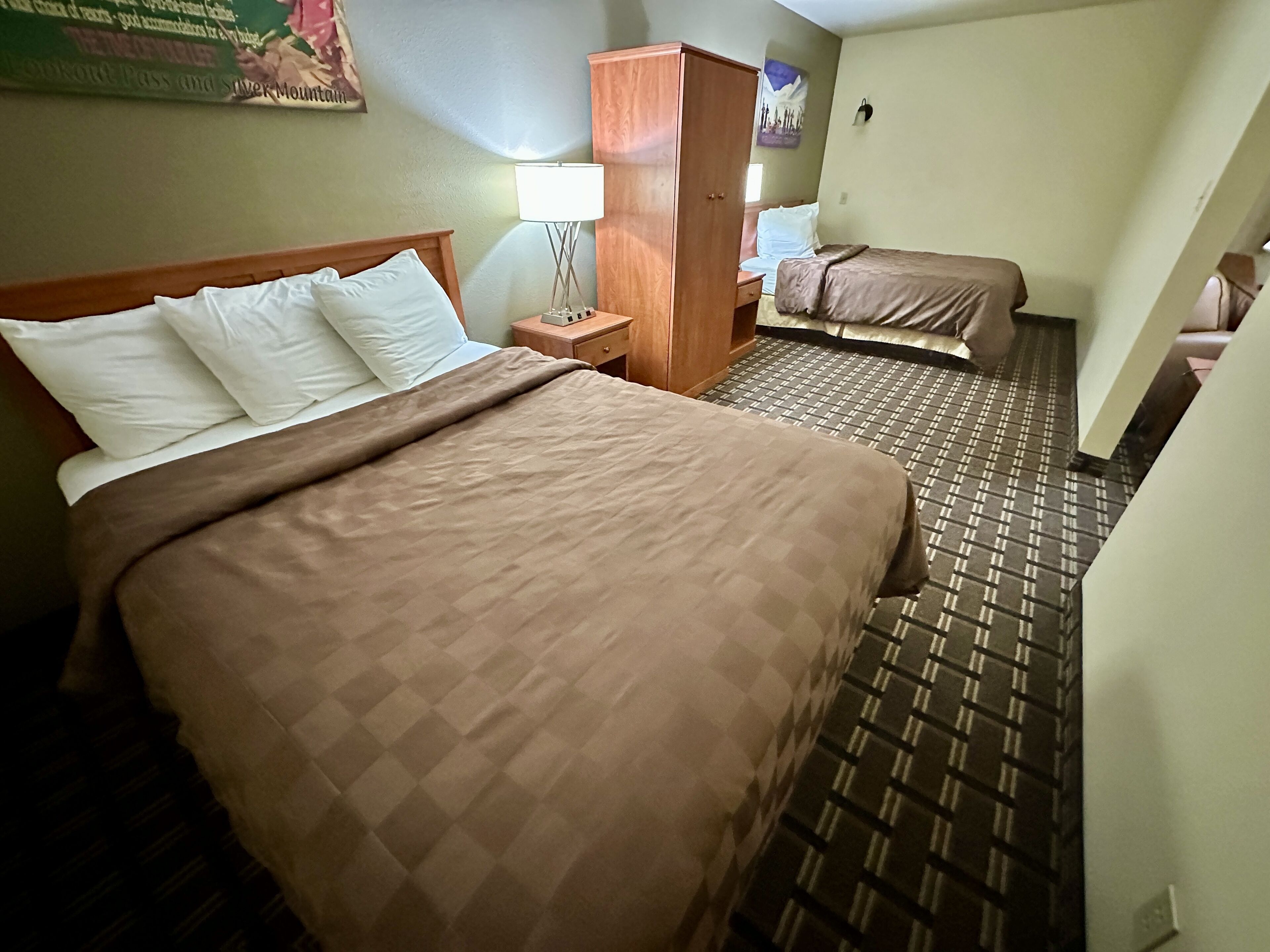 A hotel room with a large bed, a nightstand, a wardrobe, and a small desk.