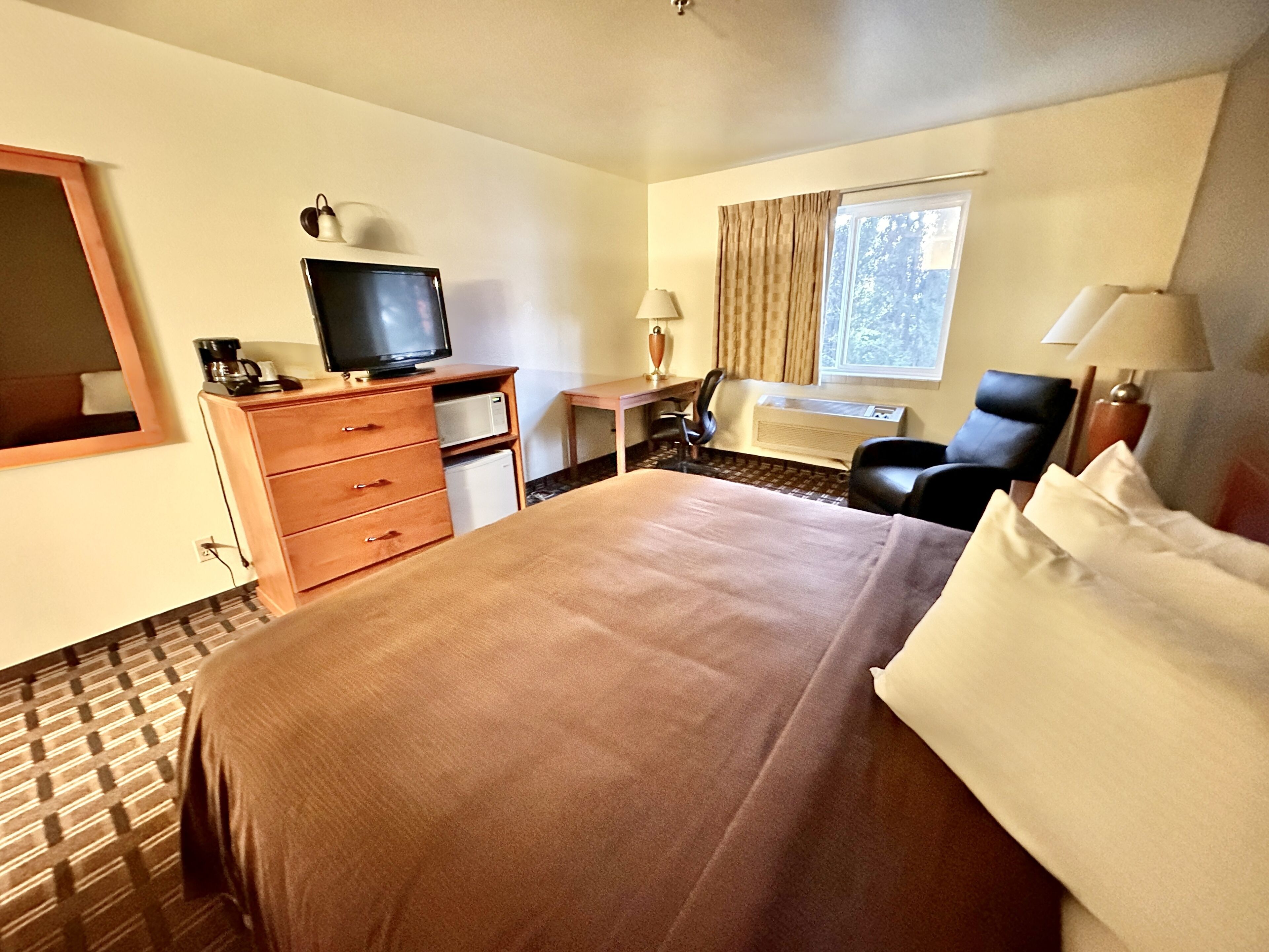 Habitación de hotel con una cama grande, un escritorio con televisor, una silla y una ventana con cortinas.