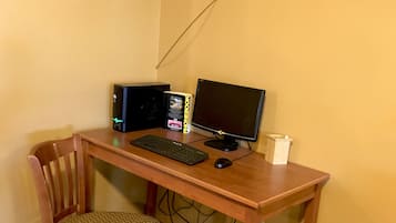 Een houten bureau met een computeropstelling, inclusief een monitor, toetsenbord en muis. Voor het bureau staat een stoel en aan de muur hangt een ingelijst fotoprint.