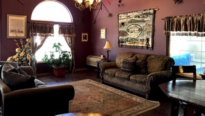 Una sala de estar con sofá, mesa de centro, candelabro y un amplio ventanal con cortinas.