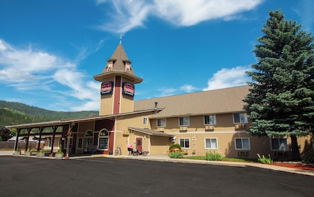 A motel with a central tower, a covered parking area, and a mountain backdrop.