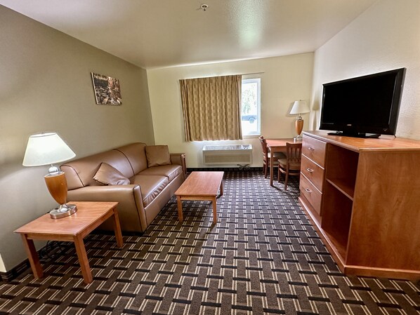 Habitación de hotel con sofá, una mesita, televisión, escritorio y ventana con cortinas.