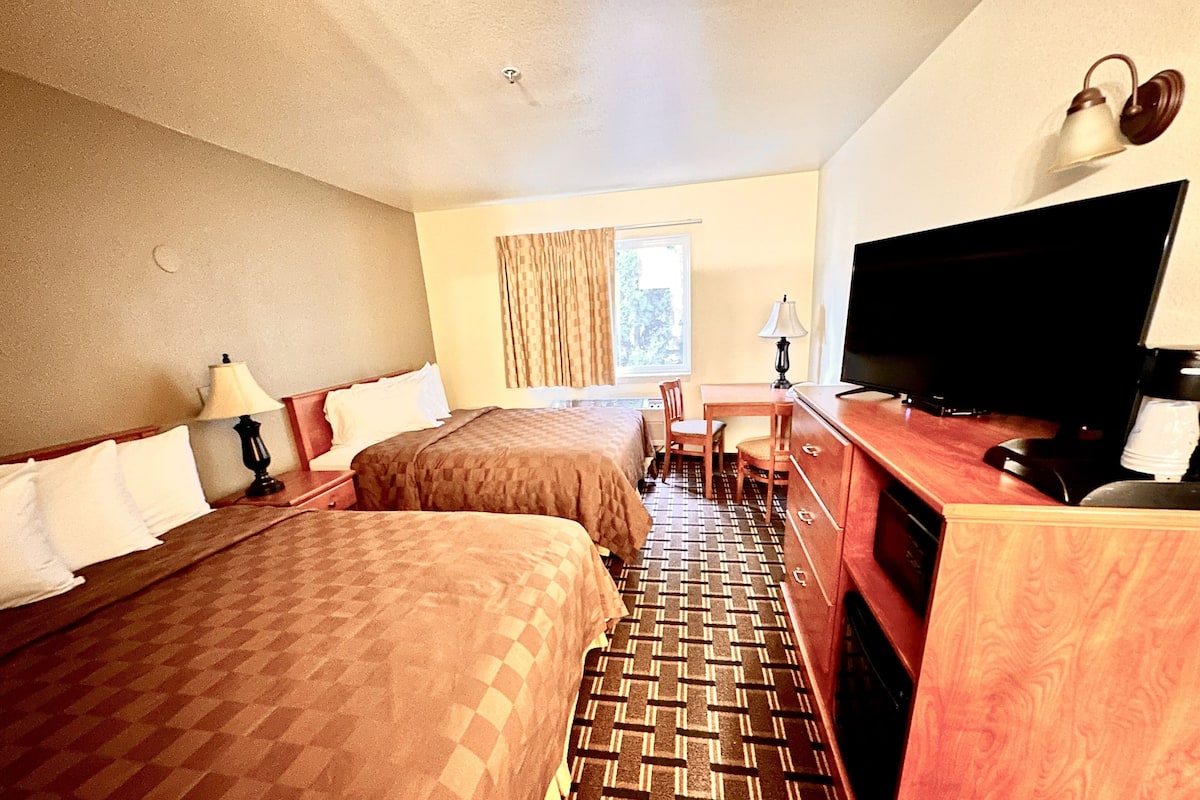 Habitación de hotel con dos camas, un escritorio, un televisor y una ventana con cortinas.