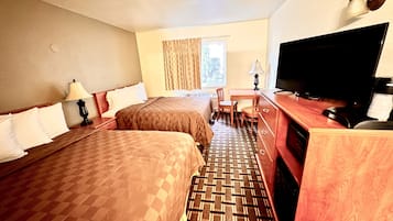 A hotel room with two beds, a desk, a television, and a window with curtains.