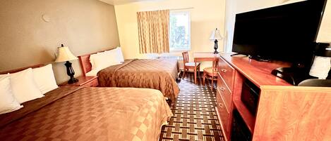 A hotel room with two beds, a desk, a television, and a window with curtains.