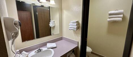 A bathroom with a sink, mirror, towel rack, and a shower area.
