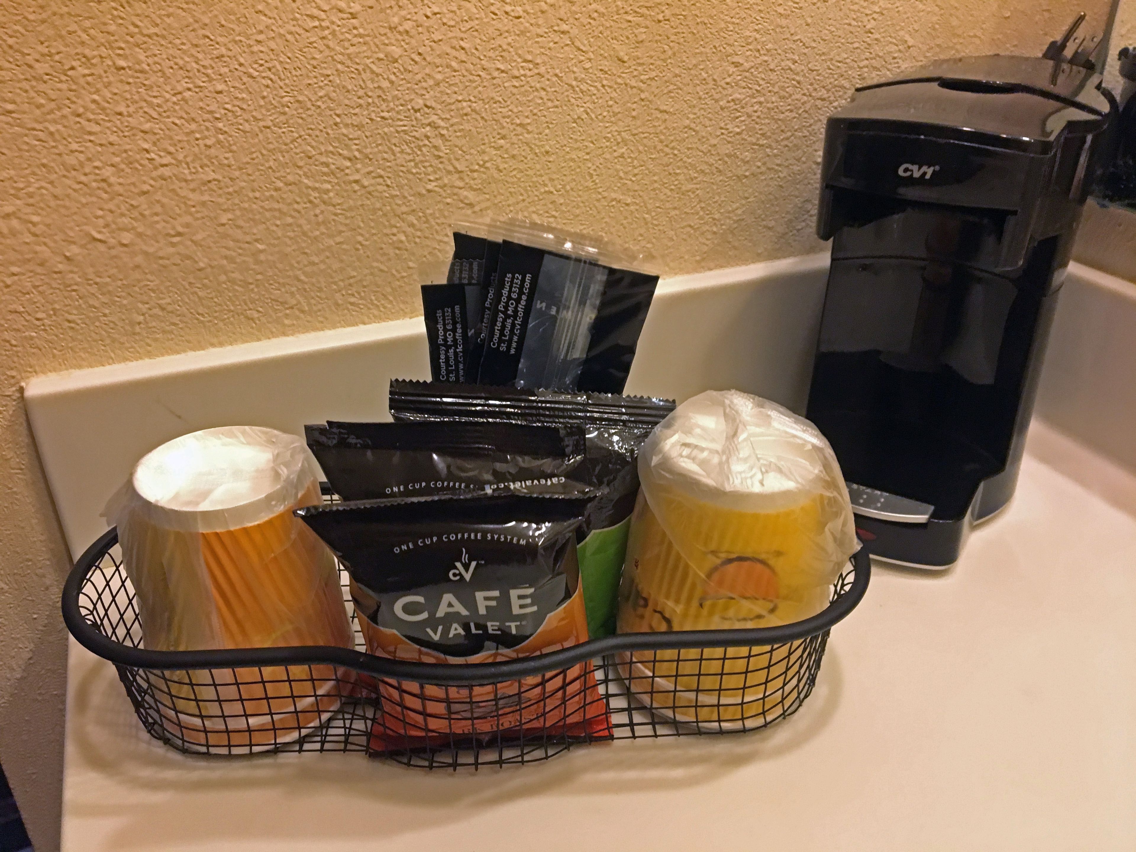 Een koffiezetapparaat, een mand met koffiekapsules, en een koffiemolen op een aanrecht.
