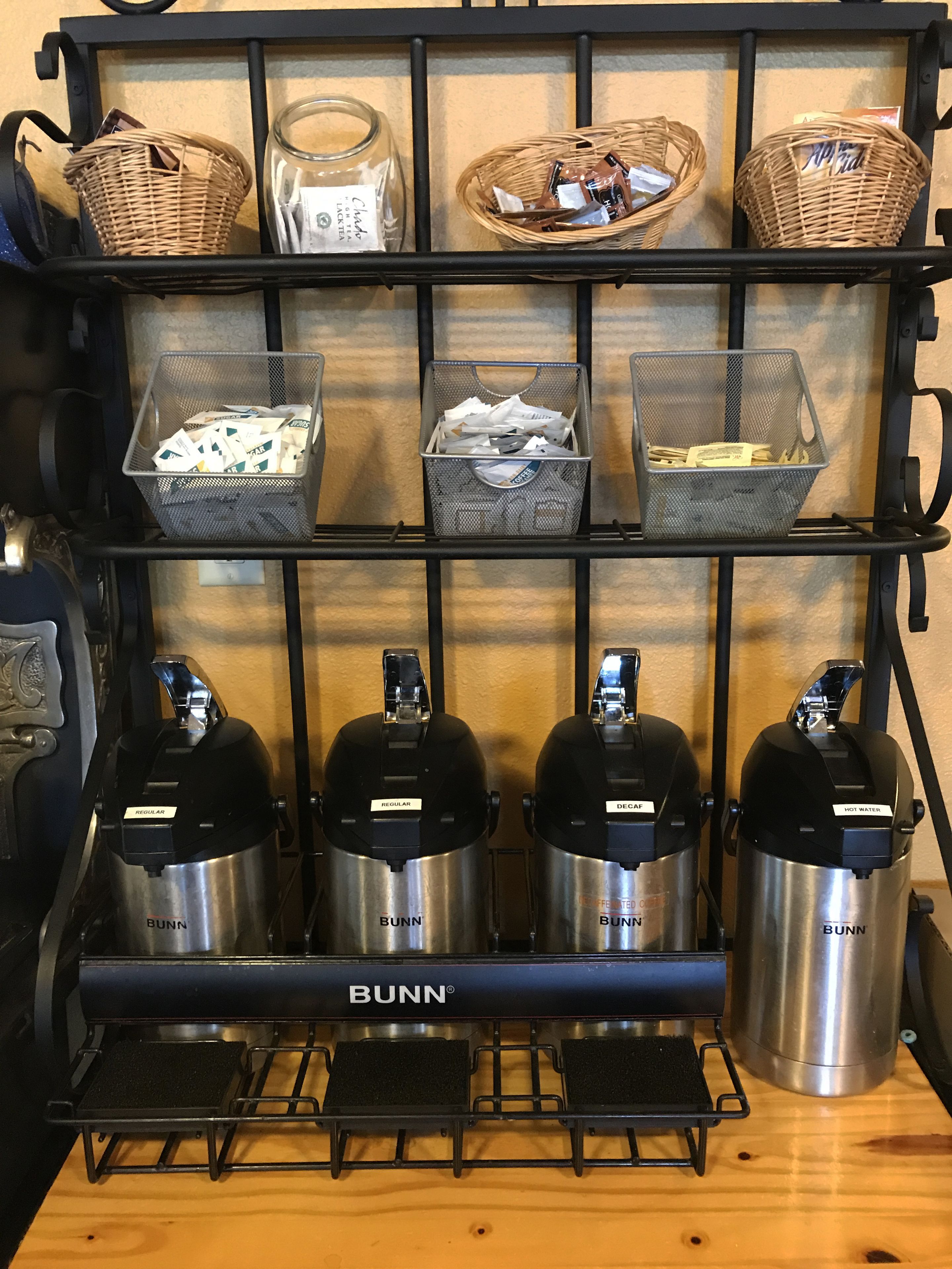 A coffee station with three Bunn coffee makers, baskets of coffee pods, and a jar of creamer.