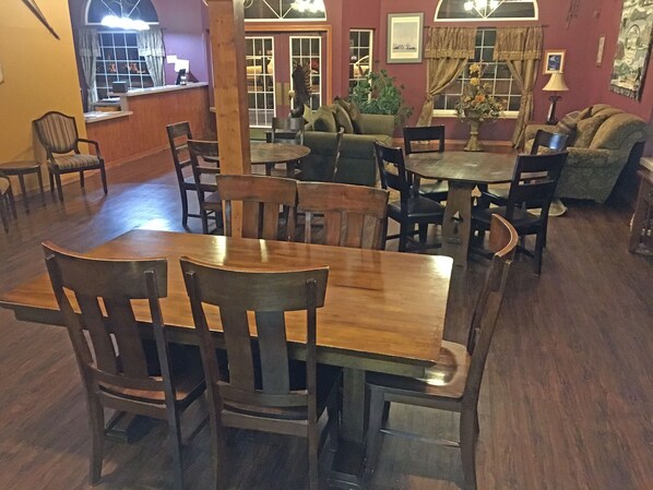 Un comedor con mesas y sillas de madera, un sofá y una zona de bar con mostrador y taburetes.