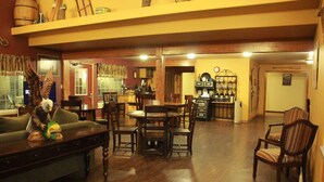 Amplia sala de estar con piso de madera, una mesa de comedor y varias sillas. Se observa una zona de bar al fondo con botellas y un refrigerador.