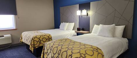 A hotel room with two beds, each with a patterned bedspread, a nightstand with a clock, and a large wall-mounted mirror.