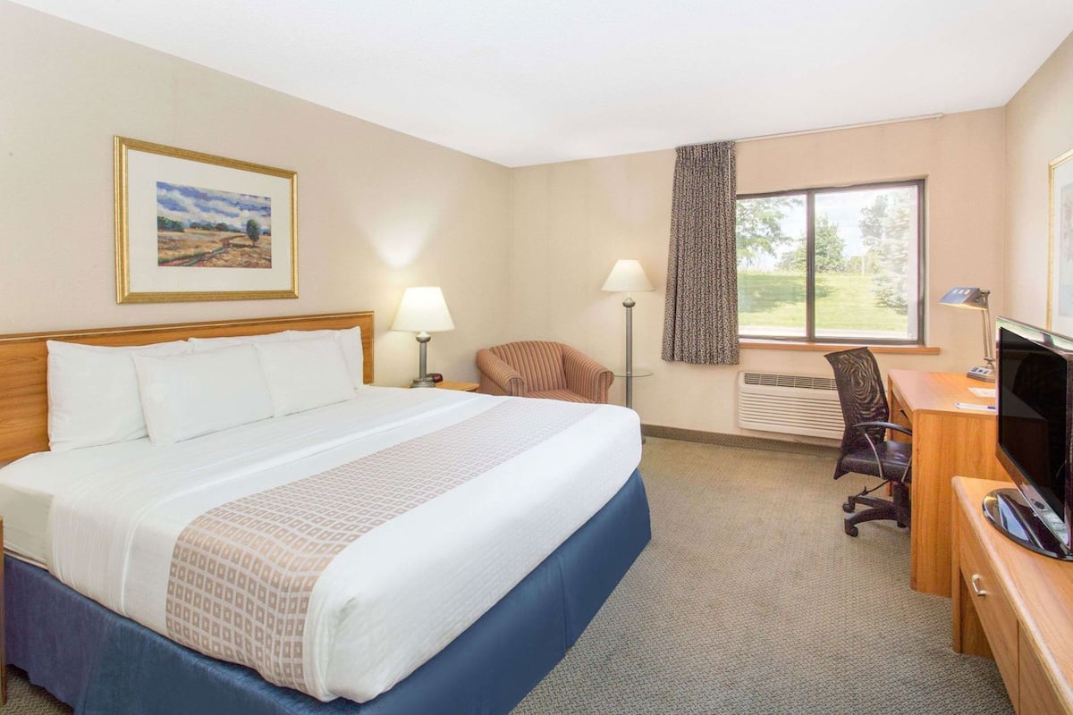 A hotel room with a large bed, a desk with a computer, a chair, a TV, and a window with a view of trees.