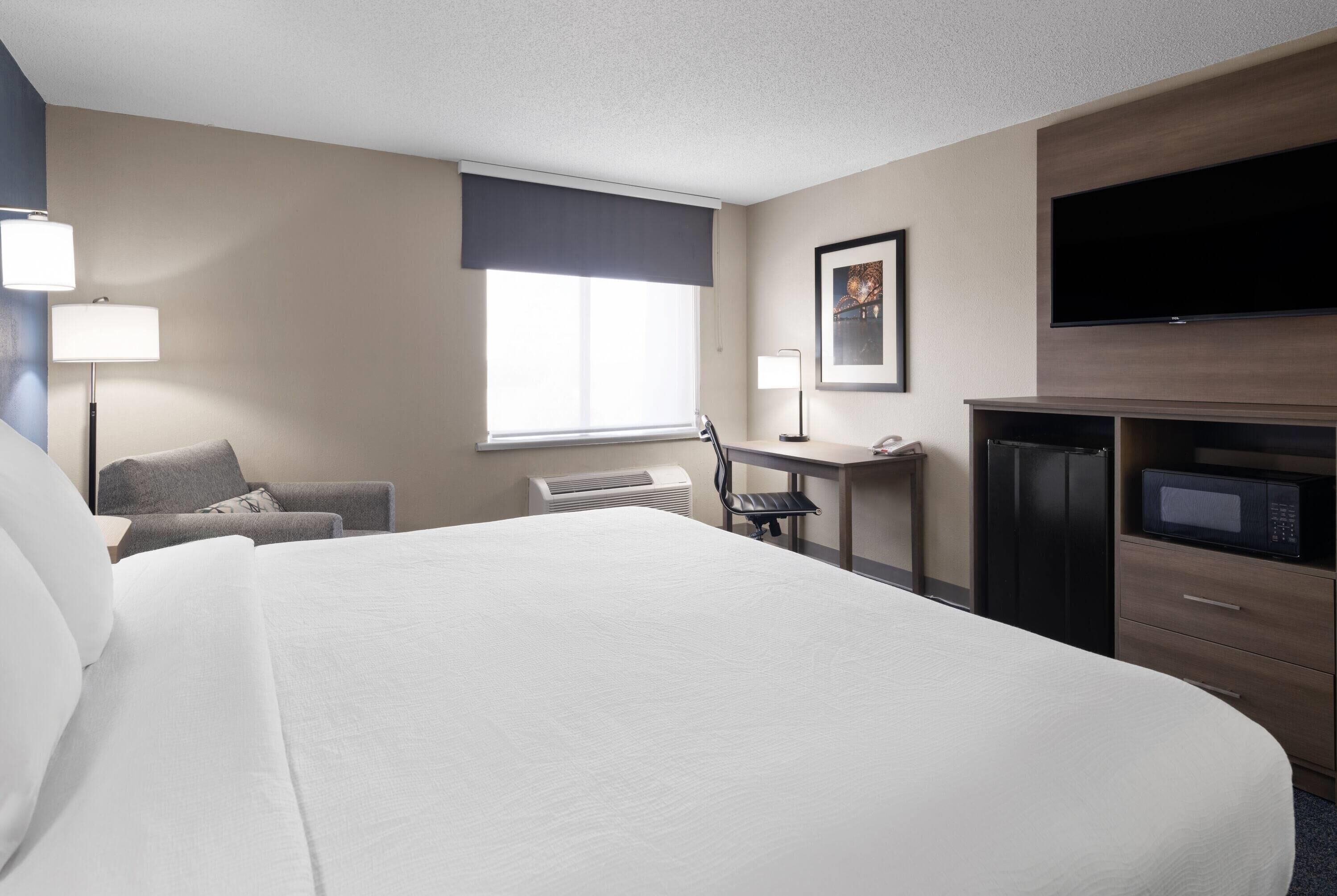 Une chambre d’hôtel équipée d’un grand lit, d’un bureau, d’une chaise, d’une télévision et d’un four à micro-ondes.
