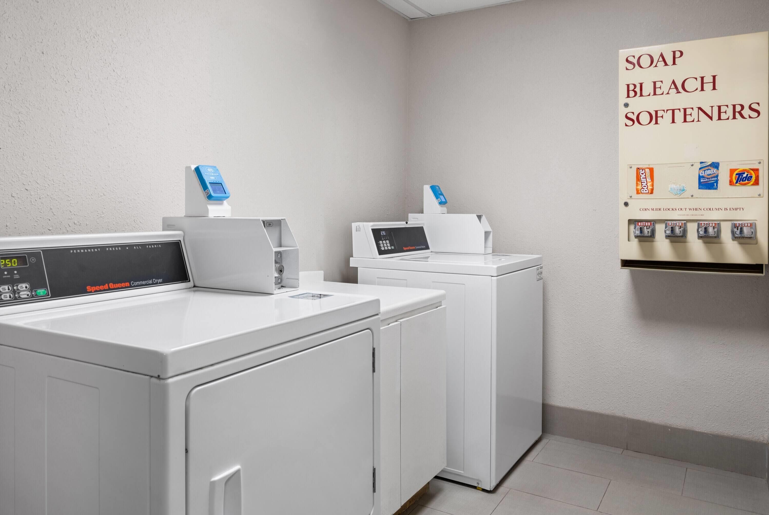 Un área de lavandería con dos lavadoras, una balanza digital y un dispensador de jabón, lejía y suavizante.