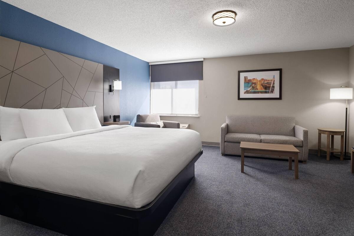 A hotel room with a large bed, a sofa, a small table, a lamp, and a picture on the wall.