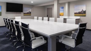 A conference room with a long table, white chairs, and a flat-screen TV on the wall.