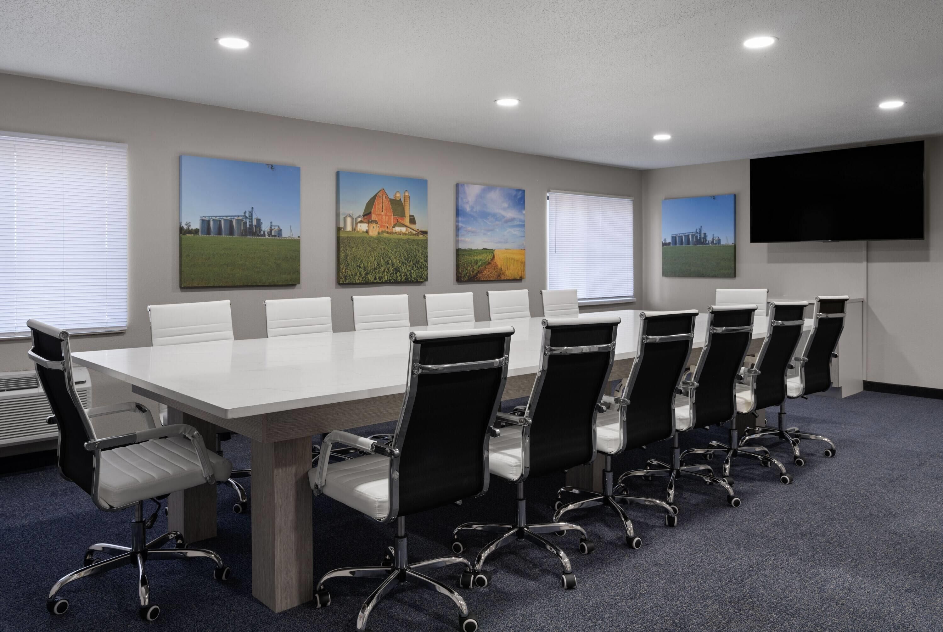 Ein Konferenzraum mit einem langen Tisch, mehreren Stühlen und einer großen Leinwand.