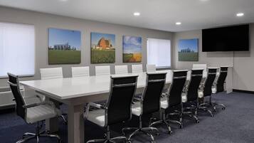 Ein Konferenzraum mit einem langen Tisch, mehreren Stühlen und einer großen Leinwand.