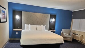 A hotel room with a large bed, two bedside tables, a chair, and a wall-mounted air conditioner.