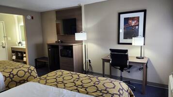 A hotel room with two beds, a desk, a chair, a microwave, a television, and a framed picture on the wall.