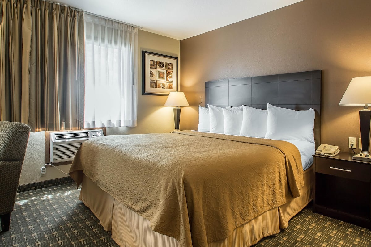 A hotel room with a large bed, two bedside lamps, a nightstand, and a chair.
