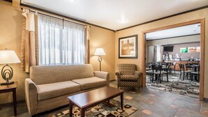 A living room with a sofa, coffee table, patterned rug, and a chair. There is a dining area visible through an open door. - Quality Inn & Suites Decorah (Decorah)